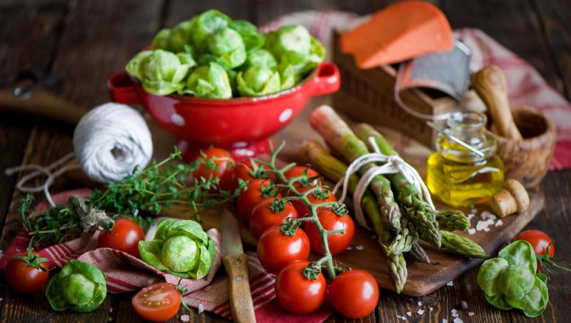 Wooden table covered in vegetables, olive oil, and cooking utensils
