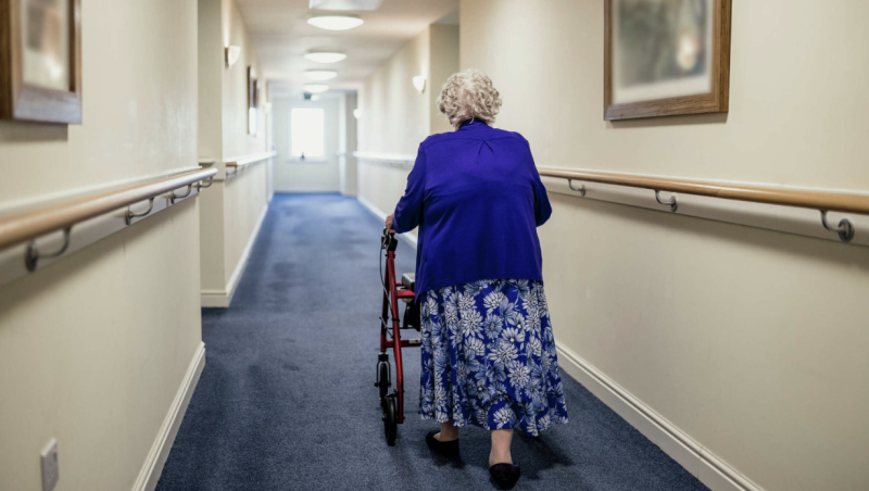 Older woman using walker in blue sweater and blue patterned skirt