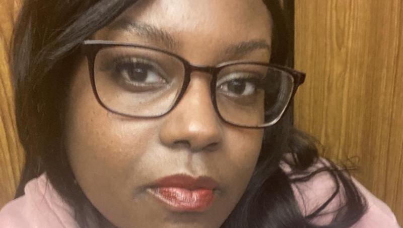 Black woman with glasses. She's wearing a pink hoodie.