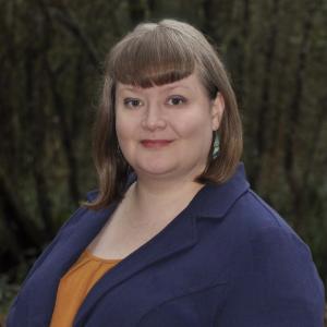 a photo of a woman with an orange shirt and a dark blue blazer.